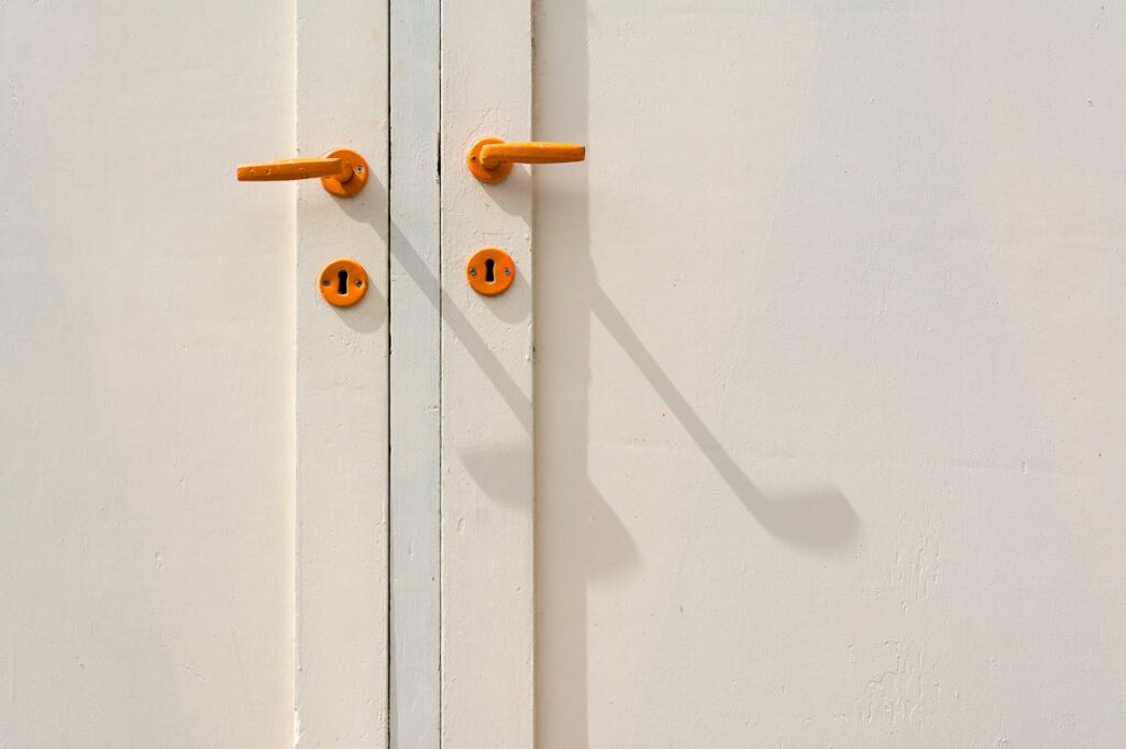 pexels-photo-13364723 Minimalist close-up of a white door featuring orange handles and shadows, creating modern aesthetic.
